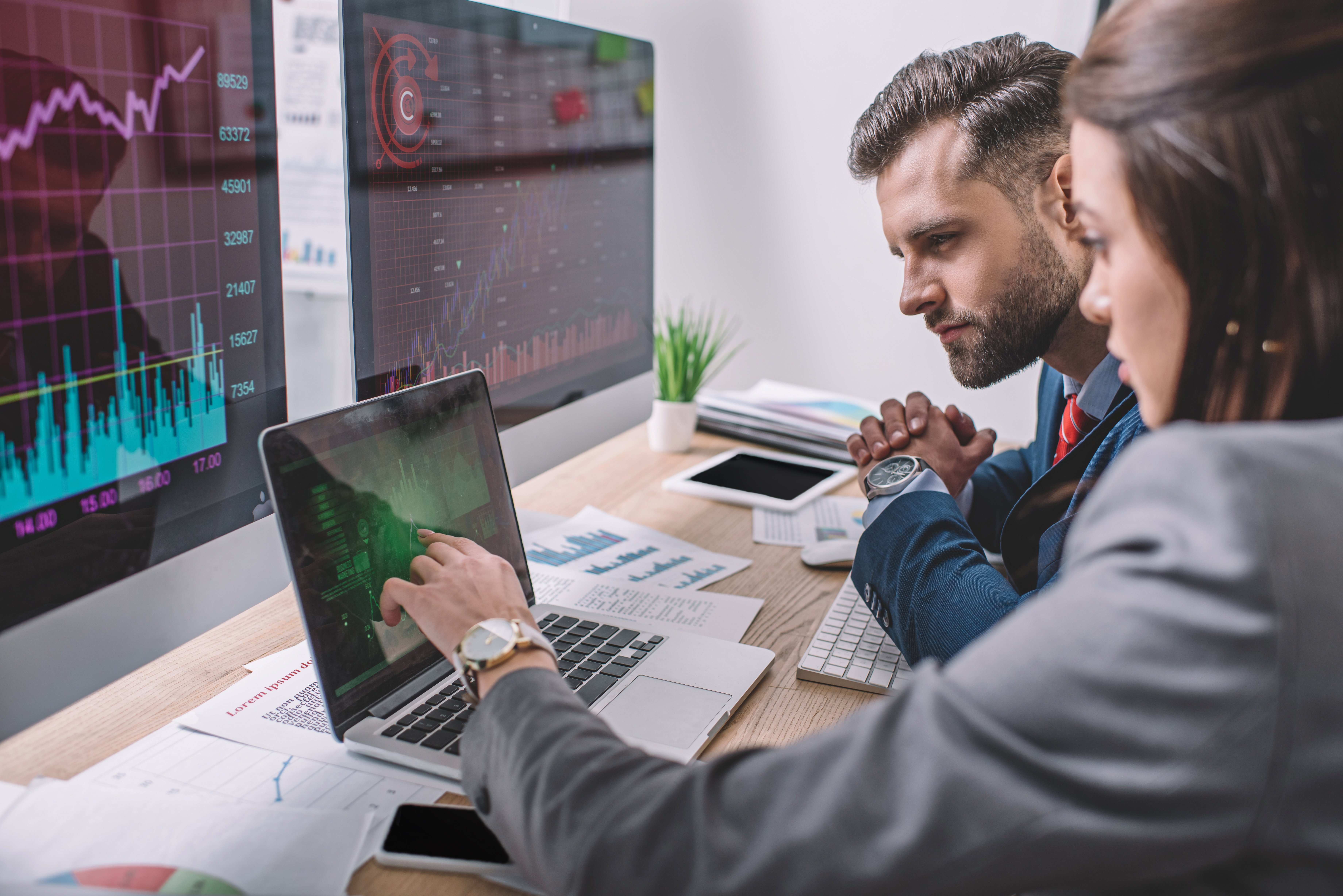 Side view of computer systems analysts using charts on computer monitors while working in office